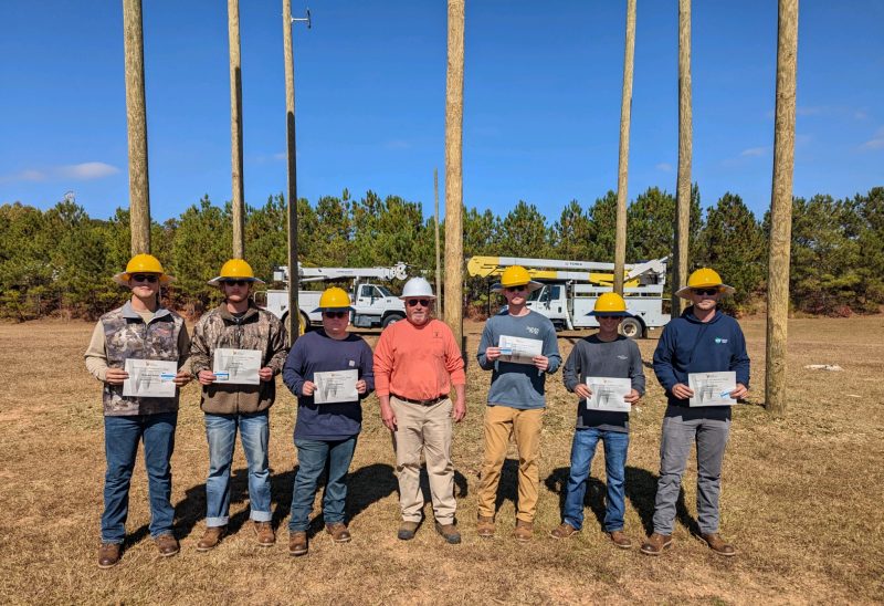 lineman graduates standing with certificates and hardhats